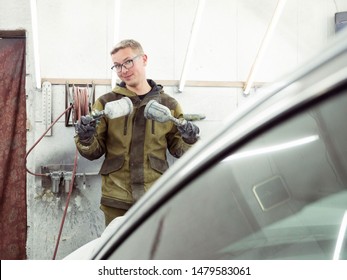 Cute Guy In Black Glasses With Black Gloves Displays The Shape Of The Hood For The Subsequent Painting Of The Car. Guy - A House Painter Working On A Car In The Garage