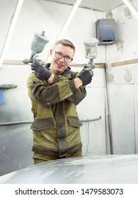 Cute Guy In Black Glasses With Black Gloves Displays The Shape Of The Hood For The Subsequent Painting Of The Car. Guy - A House Painter Working On A Car In The Garage