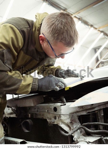 Cute guy in black glasses\
with black gloves displays the shape of the hood for the subsequent\
painting of the car. guy - a house painter working on a car in the\
garage
