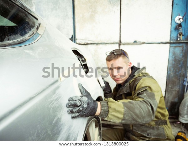 Cute guy in black glasses
with black gloves displays the shape of the hood for the subsequent
painting of the car. guy - a house painter working on a car in the
garage