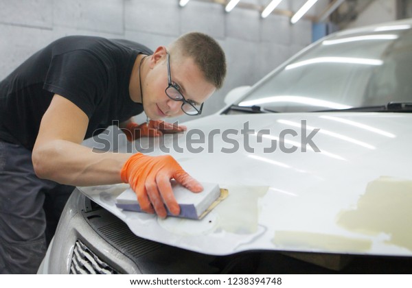 cute guy in black glasses
with orange gloves displays the shape of the hood for the
subsequent painting of the car. guy - a house painter working on a
car in the garage