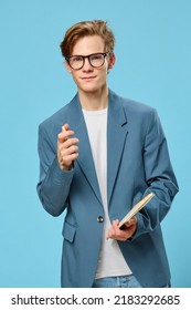 Cute Guy With Glasses And With A Notebook In His Hand Looks At The Camera