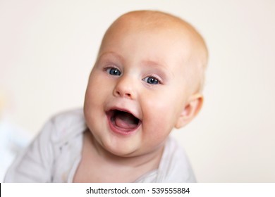 A Cute, Happy 5 Month Old Baby Girl Is Smiling A Toothless Grin At The Camera On A White Background.