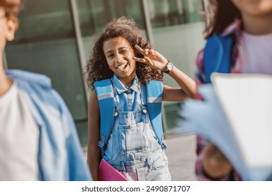 Cute happy african child preteen girl elementary middle school pupil in casual clothes with backpack going to school lessons home with fun showing peace sign gesture together with friends - Powered by Shutterstock