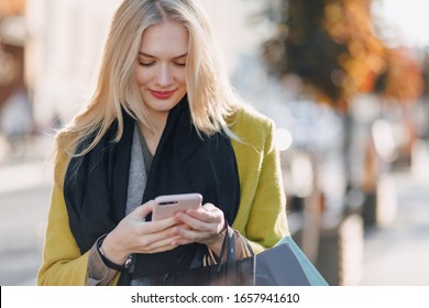 cute happy attractive blonde woman with packages on the street in sunny weather. communicates on the phone after shopping, positive emotions.
