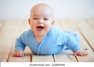 Cute Happy Baby Boy Crawling On The Wooden Deck Or Floor Lifting Itself Up On Its Hands To Laugh At The Camera