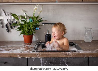 Cute Happy Baby Girl With Playing With Water, Soap Bubbles And Foam In A Kitchen Sink At Home