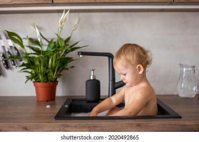 Cute Happy Baby Girl With Playing With Water, Soap Bubbles And Foam In A Kitchen Sink At Home