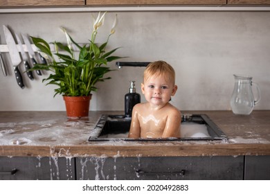 Cute Happy Baby Girl With Playing With Water, Soap Bubbles And Foam In A Kitchen Sink At Home