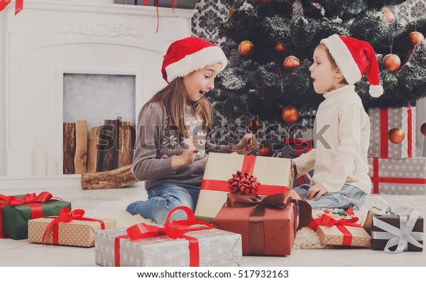 Cute happy excited children, boy and girl in santa hats unwrap ... pic