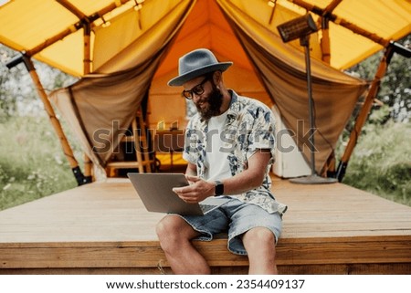 Cute happy freelancer guy using laptop on a sunny day away from the city on a campsite with free wifi. Lifestyle concept. Stay connected. Remote work in nature