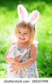 Cute Happy Girl With A Real Easter Bunny Wearing Ears At Spring Green Grass