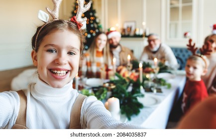 Cute happy girl in reindeer antlers taking selfie of her large family sitting at festive dining table during Xmas celebration. Grandparents, young parents and children celebrating New Year together - Powered by Shutterstock