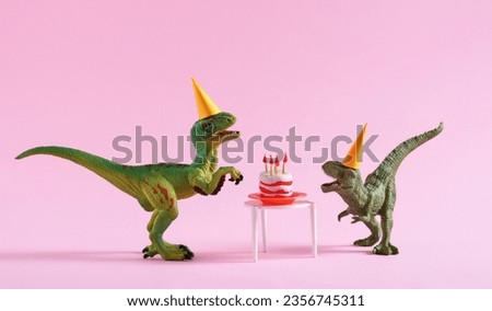 Cute happy green dinosaurs in birthday hats with cake with flaming candles on pastel pink background. Copy space. Minimal art birthday card idea.