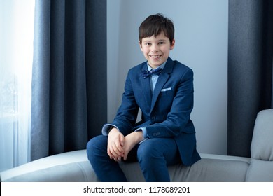 Cute Happy Junior Boy In Dark Classic Suit Outdoors. Children Portrait. Stylish Kid In Suit