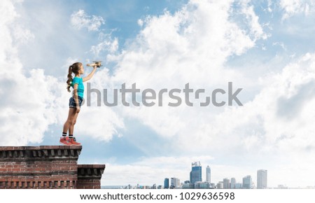 Cute happy kid girl on building top playing with retro plane model