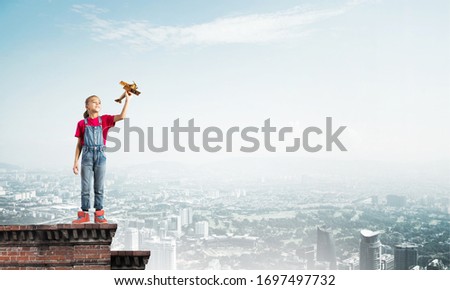 Cute happy kid girl on building top playing with retro plane model