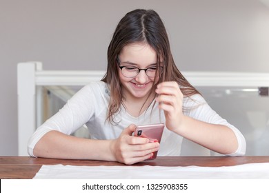 Cute happy laughing tween girl in glasses looking at smartphone in her hands talking on video call with smile. Child and gadget concept. Internet and social networks communication.