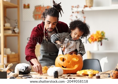 Cute happy little african american boy carving Halloween pumpkin with father at home, mixed-race family son and dad making Jack-o-Lantern together while preparing decorations for Saints Day party Foto stock © 