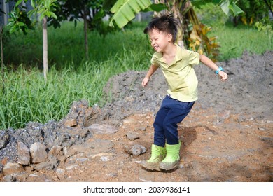 Cute Happy Little Asian 5 Years Old Kindergarten Boy Kid Wearing Green Boots Jump In Muddy Puddles At Home Backyard On Nature, Outdoor Fun In The Rain Weather