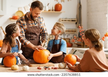 Cute happy little boy helping his father to carve Halloween pumpkin while standing in kitchen at home and preparing for autumn holiday, family son and dad making Jack-o-Lantern together