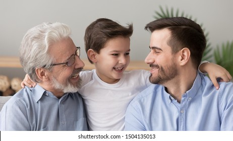 Cute happy little boy son grandson embracing young father and old elder grandfather laughing hugging at home, multi three 3 generation men family grandparent parent and grandchild bonding together