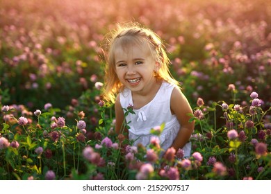 A cute happy little girl in a field with clover flowers is laughing merrily. Beautiful Pink sunset. A happy genuinely jolly child. Funny emotional kid. World Children's Day
