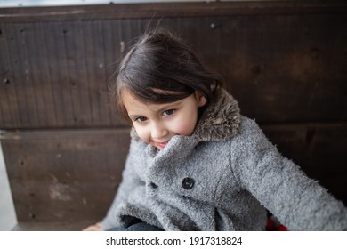 Cute and happy little girl in gray coat with strawberry syrup stain on her cheek. Adorable young child making funny faces with wooden wall as background. Kids having fun - Powered by Shutterstock