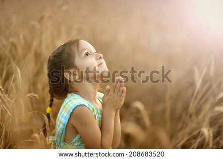 Cute happy little girl prays in wheat field