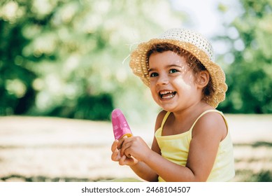 Cute happy little girl in yellow dress eating fruit ice cream. Summer fun child play in park. Summertime vibrant color background. - Powered by Shutterstock