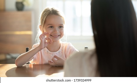 Cute happy little preschooler girl child make hand gesture learning sign language with mom or nanny, smiling small disabled kid practice nonverbal talk have lesson with teacher or tutor at home