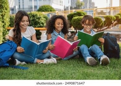 Cute happy little preteen children elementary middle school pupils schoolmates with backpacks and notebooks sitting at the grass park outdoors doing homework together - Powered by Shutterstock