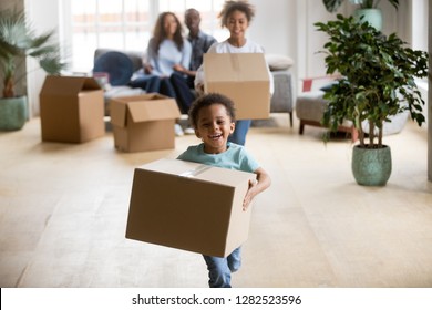 Cute Happy Mixed Race Children Enjoying Moving Day Running Carrying Holding Boxes, Excited African American Kids Laughing Playing In New Home Having Fun Unpacking, Black Family Relocation Concept