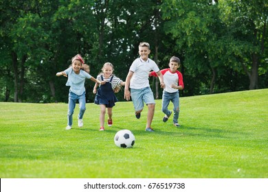 Cute happy multiethnic kids playing soccer with ball in park