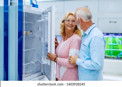 Cute Happy Smiling Caucasian Senior Choosing New Refrigerator For Their Home. Tech Store Interior.