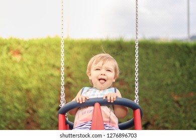 Cute Happy Smiling Little Child Having Fun Riding On Swing At Children Playground On Sunny Summer Day With Hig Tounge Out. Carefree Childhood. Copy Space. Close-up Portrait