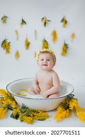 a cute happy smiling one year old baby kid girl in yellow wreath is having a milky bath in washbowl
with mimosa. Happy childhood concept and popular baby photo shoot idea