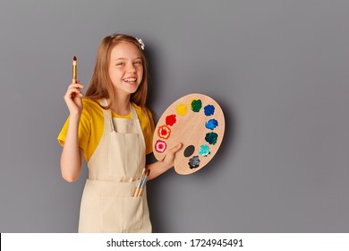 Cute Happy Teen Girl With Paint Palette And Brush On Grey Background.