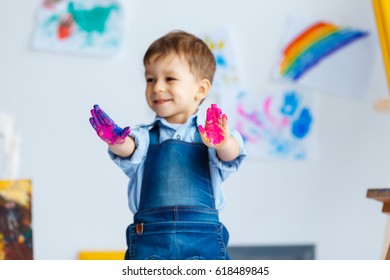 Cute, Happy, White, Three Year Boy In Blue Shirt And Jeans Showing His Dirty Hands In Watercolors. Little Child Having Fun After Painting. Concept Of Early Childhood Education, Happy Family, Parenting