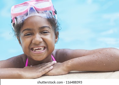 A cute happy young African American girl child relaxing on the side of a swimming pool smiling & wearing pink goggles - Powered by Shutterstock