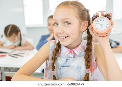 Cute Happy Young Girl Smiling Joyfully Holding Alarm Clock Sitting In The Classroom At School Studying Learning Education Timing Management Time Emotions Positivity Intelligence Examination Knowledge