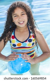 A cute happy young mixed race African American girl child playing in a swimming pool smiling with a blue ball