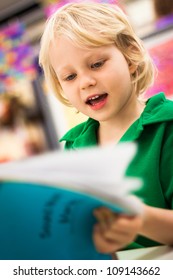 A Cute Happy Young School Boy Reading A Book In A Class Room.