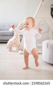 a cute healthy baby boy in a spacious bright children's room at home with a wigwam, soft toys, children's textiles. The child takes the first steps, learns to walk by himself