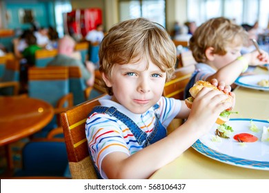 Cute Healthy Preschool Kid Boy Eats Hamburger Sitting In School Or Nursery Cafe. Happy Child Eating Healthy Organic And Vegan Food In Restaurant. Childhood, Health Concept