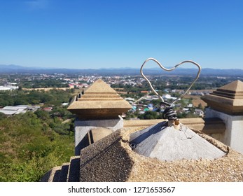 A cute heart-shaped wire on a pole projecting to a clear blue sky with landscape 