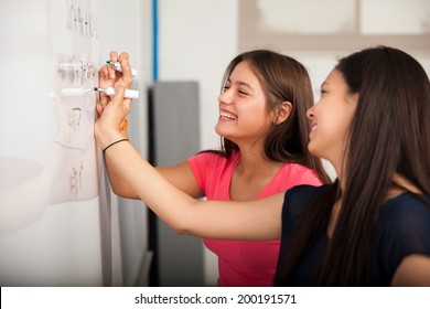 Cute high school friends laughing and having fun while solving a problem on a white board