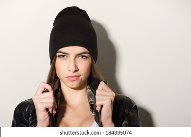 Cute hipster teenage girl with black beanie hat posing looking at camera against white wall. Copy space available. 