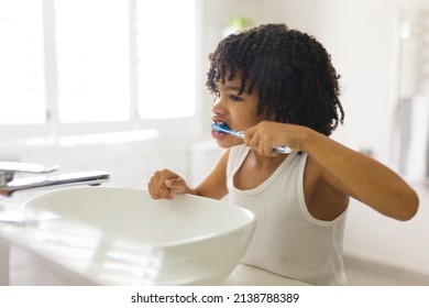 Cute Hispanic Boy Brushing Teeth By Sink In Bathroom At Home. Unaltered, Childhood, Hygiene And Routine Concept.