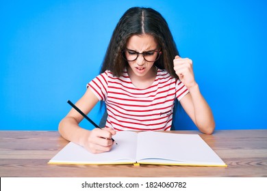 Cute Hispanic Child Girl Sitting On The Table Writing Book Annoyed And Frustrated Shouting With Anger, Yelling Crazy With Anger And Hand Raised 